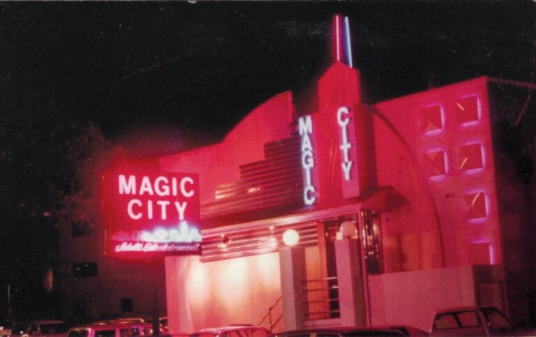 A night view of the Magic City building illuminated in bright pink and red neon light.